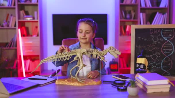 デニムシャツで自然科学を学ぶ少女は 自宅で骨からチラノサウルスのモデルを作っています 子供の頃のコンセプトと学校での勉強 — ストック動画