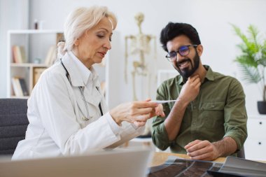 Kafkas kıdemli kadın doktor ve boğazı ağrıyan genç erkek modern tıp merkezinin masasında oturmuş ve sıcaklığı ölçüyorlar..