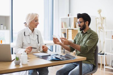 Kıdemli kadın pratisyen doktor yeni klinikte elinde şişeyle genç bir hastayla iletişim kuruyor. Doktor sağlık sorunlarını tartışıyor ve laptoptaki tıbbi verileri inceliyor..