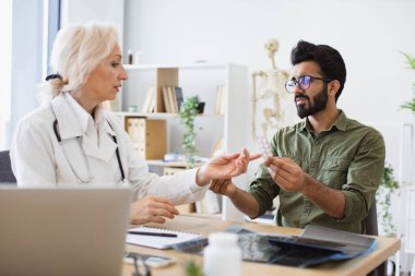 Doktor sağlık sorunlarını tartışıyor ve laptoptaki tıbbi verileri inceliyor. Kıdemli kadın pratisyen doktor yeni klinikte elinde şişeyle genç bir hastayla iletişim kuruyor..