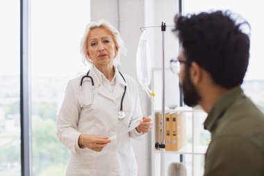 Laboratuvar önlüğü giyen yaşlı bir kadın kemoterapi için çözeltisi olan muayene odasındaki kanepede oturan genç bir adam. Klinikte kanser olan erkek hastaya danışmanlık yapan sağlık uzmanı..