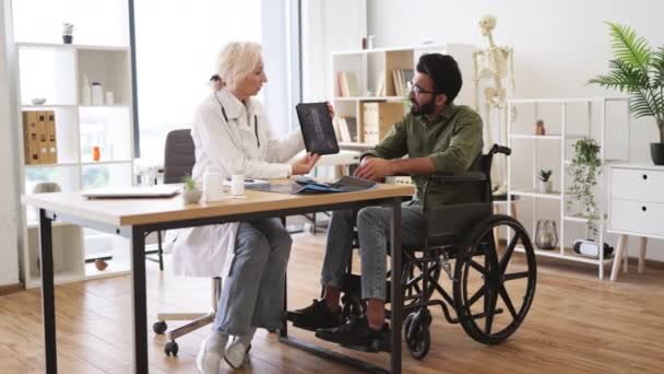 全景老年女士白色外套展示脊椎扫描石碑上的注意男人使用轮椅 有效的创伤专家让病人放心医院内部的诊断 — 图库视频影像