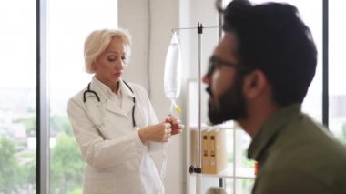 Laboratuvar önlüğü giyen yaşlı bir kadın kemoterapi için çözeltisi olan muayene odasındaki kanepede oturan genç bir adam. Klinikte kanser olan erkek hastaya danışmanlık yapan sağlık uzmanı..