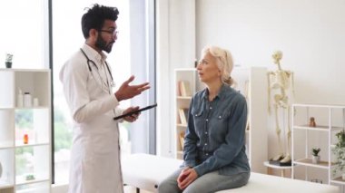 Sakallı erkek doktor ve yaşlı kadın hasta modern tıp merkezinin muayene koltuğunda oturuyor ve hastalık teşhisi koyuyor. İlaçları doğru almak için genç uzman yazarlık eğitimi.