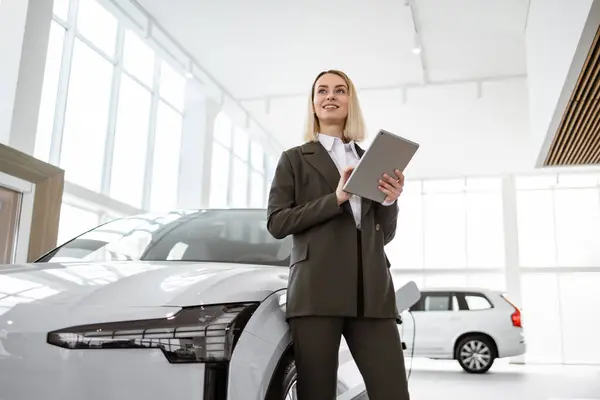 stock image Professional smiling female car dealer posing at auto showroom holding tablet pc. Happy saleswoman working at automobile dealership, copy space. Professionalism, management concept.