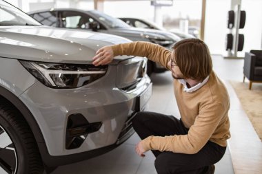 Adam alıcının yandan görünüşü, günlük giysiler içinde araba seçen bir müşteri, yeni bir araba almak istiyor. Galeri araç galerisinde araba farlarına dokunan kendine güvenen bir müşteri. Satış konsepti.