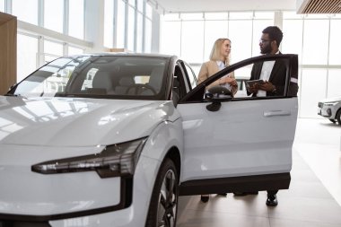 Potansiyel alıcıya otomobilini gösteren kendine güvenen bir adam, açık kapıları olan bir araba kulübesine bakıyor. Afrikalı erkek araba satıcısı galeri müşterisiyle birlikte galeride duruyor. Yönetici istemci ile çalışıyor.