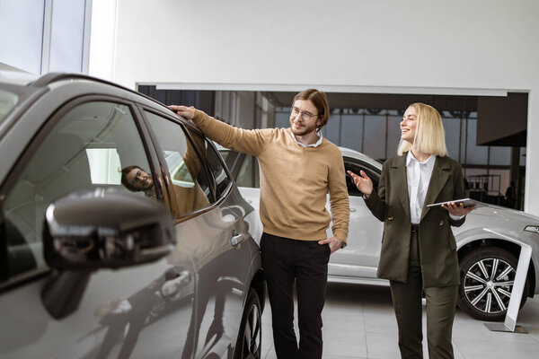 Успешный бизнесмен в автосалоне, продажа автомобилей клиентам. Профессиональная женщина-консультант предоставляет всю информацию о новом автомобиле с помощью планшета кавказскому клиенту в автосалоне.