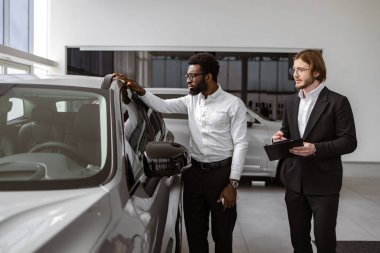 Profesyonel Kafkasyalı danışman, araba galerisindeki Afrikalı erkek müşterilere dosya kullanarak yeni araba hakkında bilgi sağlıyor. Araba galerisinde başarılı bir işadamı, müşterilere araç satışı