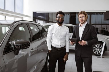Profesyonel Kafkasyalı danışman, araba galerisindeki Afrikalı erkek müşterilere dosya kullanarak yeni araba hakkında bilgi sağlıyor. Araba galerisinde başarılı bir işadamı, müşterilere araç satışı