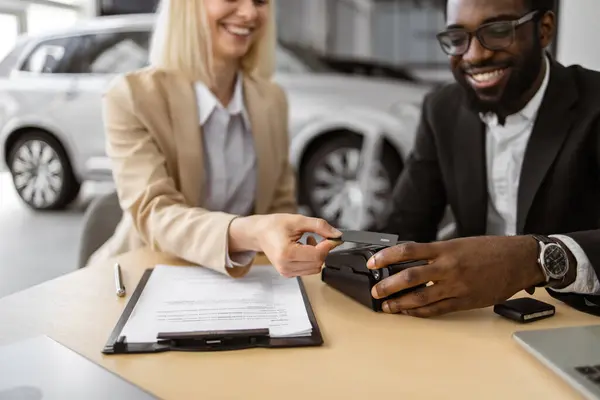 新しいモダンな車を購入するために端末で電子クレジットカードで支払う若い女性の手のクロップビュー アフリカのマネージャーは ブランドクロスオーバーの購入のための女性の顧客の支払いを支援 ストックフォト