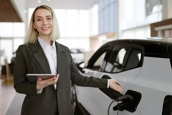 Young Blond Caucasian Saleswoman Selling Electric Cars Light Modern Showroom Stock Picture
