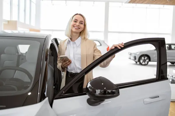 ライトカーサロンのディーラー店で自動車を購入する若い女性 パノラマウィンドウ付きショールームで新しい車を選択する正式な着用で広範なビジネスマンのバイヤー セールスコンセプト ロイヤリティフリーのストック写真