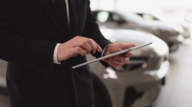 Elinde dijital tablet olan takım elbiseli genç araba satıcısının görüntüsü. Kendine güvenen sakallı adam modern aletlerle yeni bir araba almak için emir veriyor..