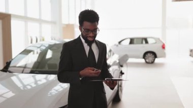 Afrikalı satıcı, galerideki yeni arabanın anahtarını müşteriye veriyor. Araba satıcısı neşeyle gülümsüyor, anahtarı tutuyor, satılık yeni araçların önünde duruyor. Teklif, indirim kavramı.