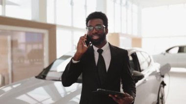 Araba satıcısı otomobil galerisinde pano tutuyor. Araba galerisinde iş görüşmesi yaparken akıllı telefon kullanan gülümseyen bir satıcı. Modern araba galerisinde çalışan kendine güvenen profesyonel bir satış elemanı..