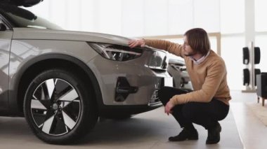 Adam alıcının yandan görünüşü, günlük giysiler içinde araba seçen bir müşteri, yeni bir araba almak istiyor. Galeri araç galerisinde araba farlarına dokunan kendine güvenen bir müşteri. Satış konsepti.