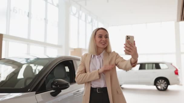 自動車サービスでスマートフォンを使用してセルフィーを取る成功したビジネスマン ハッピー笑顔の白人少女バイヤーは新しい車を買うことについてオンラインで話します — ストック動画
