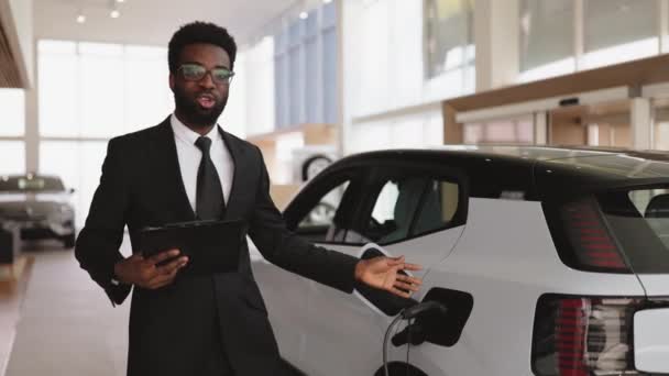 Salesman Muda Afrika Berjanggut Menjual Mobil Listrik Showroom Modern Ringan — Stok Video