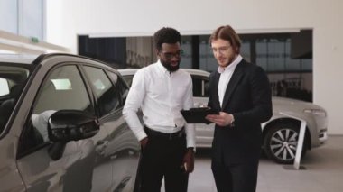 Profesyonel Kafkasyalı danışman, araba galerisindeki Afrikalı erkek müşterilere dosya kullanarak yeni araba hakkında bilgi sağlıyor. Araba galerisinde başarılı bir işadamı, müşterilere araç satışı