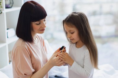 Yatak odasında oturan küçük kız annesine makyaj yapıyor. Mutlu anne ve kız hafta sonu birlikte eğleniyorlar. Kız, güzel annesine dudak boyuyor. Mutlu sevgi dolu aile.