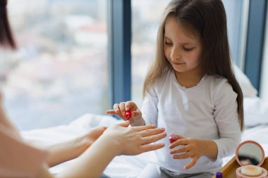 Şirin küçük kız anne ellerine oje sürerek oje sürmeyi öğreniyor. Mutlu anne ve kız yataklarında oturup manikür yapıyor, vücutlarıyla ilgileniyorlar..