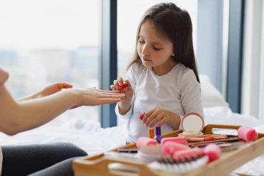 Mutlu anne ve kız yataklarında oturup manikür yapıyor, vücutlarıyla ilgileniyorlar. Sevimli küçük kız anne ellerine oje sürerek oje sürmeyi öğreniyor..