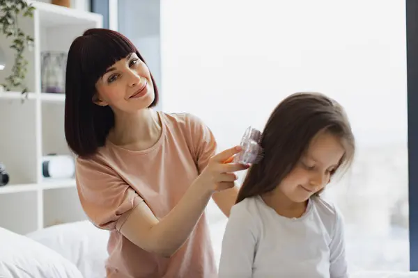 Charming Caucasian Mother Combing Her Daughters Hair While Sitting Bed Stock Picture