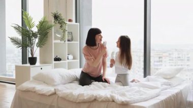 Genç anne, yatakta otururken mikrofon yerine tarak kullanarak sevimli kızıyla şarkı söylüyor. Mutlu Kafkas ailesi hafta sonu sabahı eğleniyor..