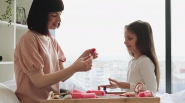 Panoramik pencerenin yanındaki yatakta güzellik günü. Annesiyle sıradan bir şekilde takılan sevimli beyaz kız tırnaklarını boyuyor. Genç anne kızına kendi başının çaresine bakmayı öğretiyor..
