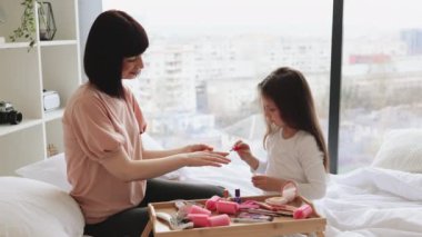 Mutlu anne ve kız yataklarında oturup manikür yapıyor, vücutlarıyla ilgileniyorlar. Sevimli küçük kız anne ellerine oje sürerek oje sürmeyi öğreniyor..