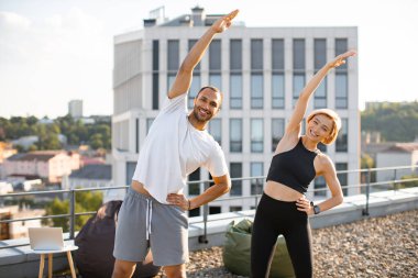 Beyaz tişörtlü pozitif adam ve siyah bluzlu kadın kollarını kaldırarak spor yapıyorlar. Mutlu spor çifti sabah sağlık jimnastiğine katılıyor..