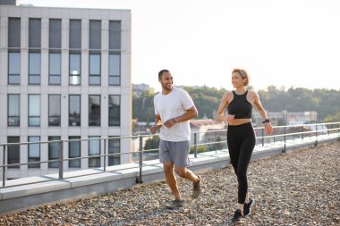 Genç spor çifti, sabahları modern binanın çatısında spor yapıyor. Mutlu erkek ve kadın sağlıklı vücut ve zihni korumak için dışarıda koşuyor..