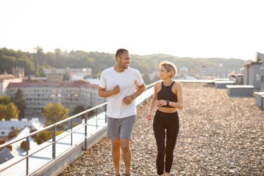 Genç güçlü bayan ve erkek sporcular sabah şehrinin arka planında koşuyorlar. Mutlu sportif çift sağlıklı yaşam tarzını teşvik ediyor..