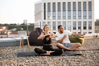 Genç mutlu çift yoga dersinden sonra modern evin çatısında dans ediyor. Atletik adam ve zayıf kadın sabah ısınması sırasında bacak bacak üstüne atarak oturuyorlar..
