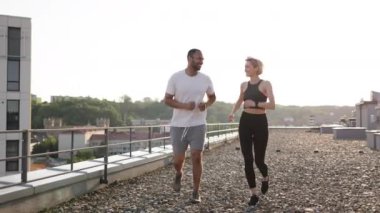 Genç spor çifti, sabahları modern binanın çatısında spor yapıyor. Mutlu erkek ve kadın sağlıklı vücut ve zihni korumak için dışarıda koşuyor..