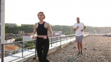 Sabahları siyah tişörtlü genç bir kadın beyaz tişörtlü bir erkekle şehir geçmişine karşı koşuyor. Sağlıklı yaşam tarzı kavramı ve günün olumlu başlangıcı.