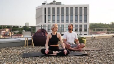 Spor giyimli genç bir çift modern evin çatısında lotus pozisyonunda minderlerin üzerinde oturuyor. Atletik bir erkek ve esnek bir kadın sabah şehir geçmişi üzerine meditasyon yapıyorlar..