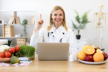 Yetişkin diyetisyen hasta için dengeli bir diyet planı hazırlıyor ya da ofis masasında çiğ sebzeler ve meyvelerle oturan müşterilere detoks ve kilo kaybı tavsiyesi veriyor.