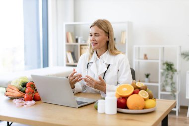 Dost canlısı, olgun bir kadın hastanedeki doktorların iş yerindeki kablosuz cihazla video görüşmesi yapıyor. Müşterilerin gıdaları tanımlamada ilerleme kaydetmeleri hakkında çevrimiçi danışmanlık sunan dikkatli dietisyen.