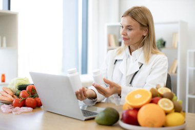 Teletıp ve teletıp konsepti. Olgun beslenme uzmanı kadın doktor, bilgisayarı kullanarak hastaya tıbbi tedaviyi bir video konferansı yoluyla açıklıyor..