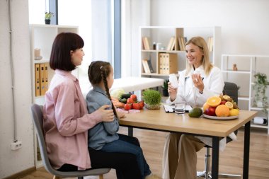 Mutlu kadın beslenme uzmanı annesinin kucağında oturan küçük kız için ilaç dolu şişeler tutuyor. Olgun çocuk doktoruna modern klinikte kadın hasta kabul edilir..