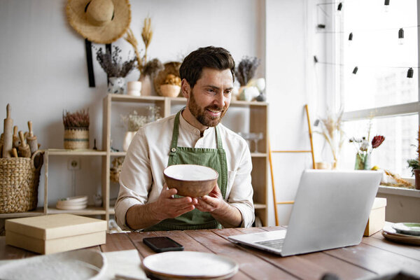 Уверенный молодой бизнесмен, управляющий творческим малым бизнесом. Взрослый владелец керамического магазина, используя ноутбук во время работы в магазине. Мужчина предприниматель, управляющий онлайн заказ кружку на сайте.
