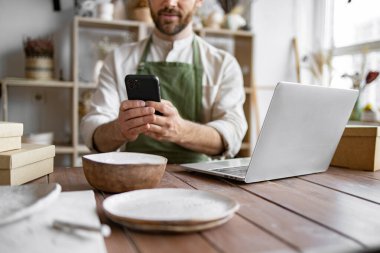 Beyaz erkek web sayfası ve sosyal medya portföyünü güncelliyor. Sakallı olgun çömlekçi kendi çömlekçisinin web sitesi için el yapımı çanak çömlek fotoğraflarını çekiyor..