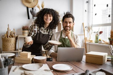 Kafkasyalı birkaç iş arkadaşı küçük çömlek imalatı işinde çalışıyor. Olgun erkek ve önlüklü genç kıvırcık saçlı kadın, mağaza sitesindeki ürünlerin envanterini çıkarmak için dizüstü bilgisayar kullanıyorlar..