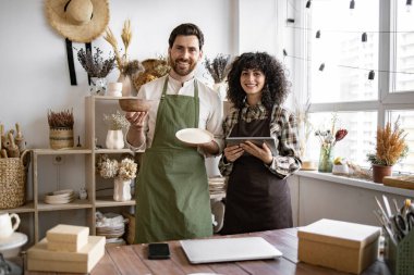 Tabletli beyaz insanlar dükkandaki stokları kontrol ediyor. Sakallı satıcı elinde seramik kâse ve tabakla dijital tablet yazan güzel bir satıcı..