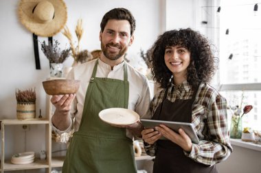Tabletli beyaz insanlar dükkandaki stokları kontrol ediyor. Sakallı satıcı elinde seramik kâse ve tabakla dijital tablet yazan güzel bir satıcı..