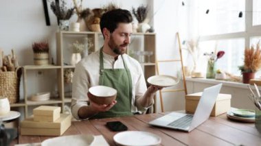 Yeşil önlük giyen çekici sakallı adam modern dekor mağazasından mal alıyor. Profesyonel satıcı kasede ve tabakta el ele tutuşan bir hasar olup olmadığını kontrol ediyor..