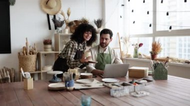 Kafkasyalı birkaç iş arkadaşı küçük çömlek imalatı işinde çalışıyor. Olgun erkek ve önlüklü genç kıvırcık saçlı kadın, mağaza sitesindeki ürünlerin envanterini çıkarmak için dizüstü bilgisayar kullanıyorlar..