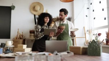 Genç kıvırcık kadın tablet kullanırken sakallı, olgun bir adam malları sayıyor. İki beyaz üniformalı işçi dekor dükkanında envanter çıkarıyorlar..